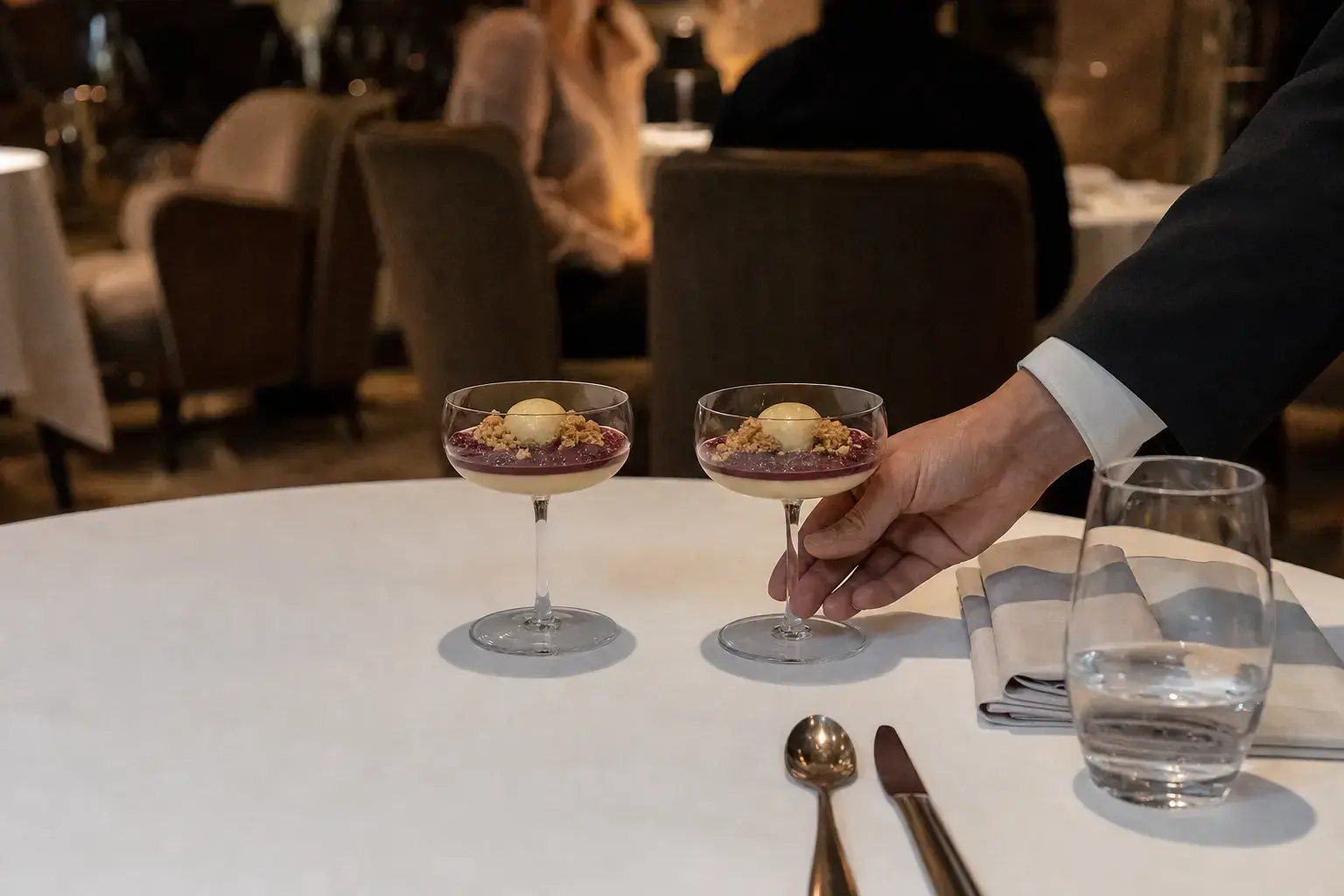Duas sobremesas idênticas servidas de uma vez no mesmo lugar da mesa do restaurante parceiro, com a mão do garçom ainda na segunda taça.