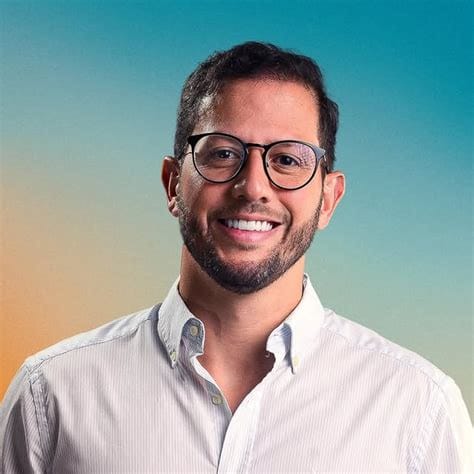 eu, Rodrigo Góes, o Mago das Milhas, de óculos e camisa listrada, num retrato de frente sobre fundo liso