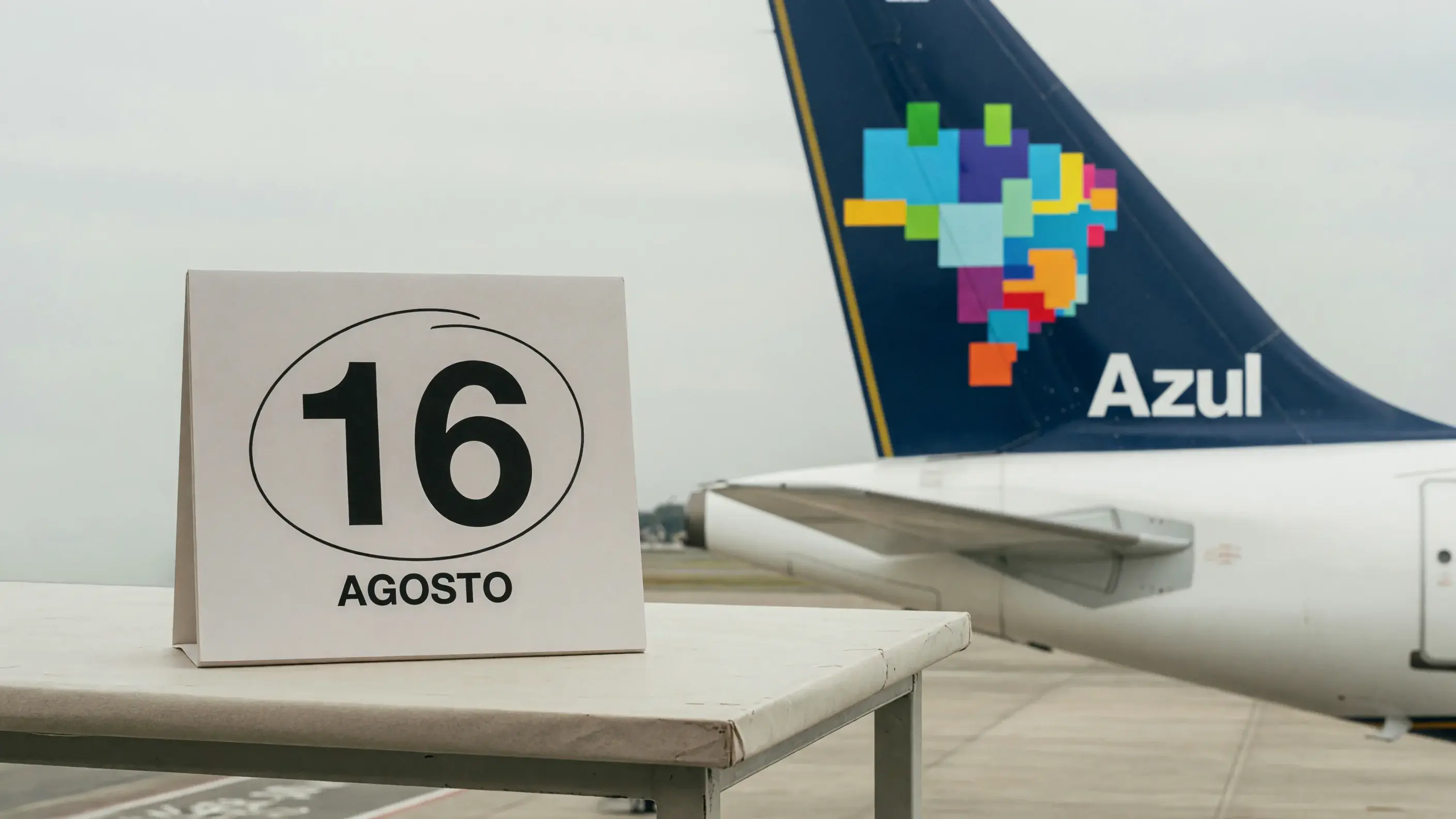 Cauda de um avião da Azul com a marca visível, ao lado de um calendário de mesa marcado em 16 de agosto — a data em que a adesão promocional ao Clube Azul se fecha.