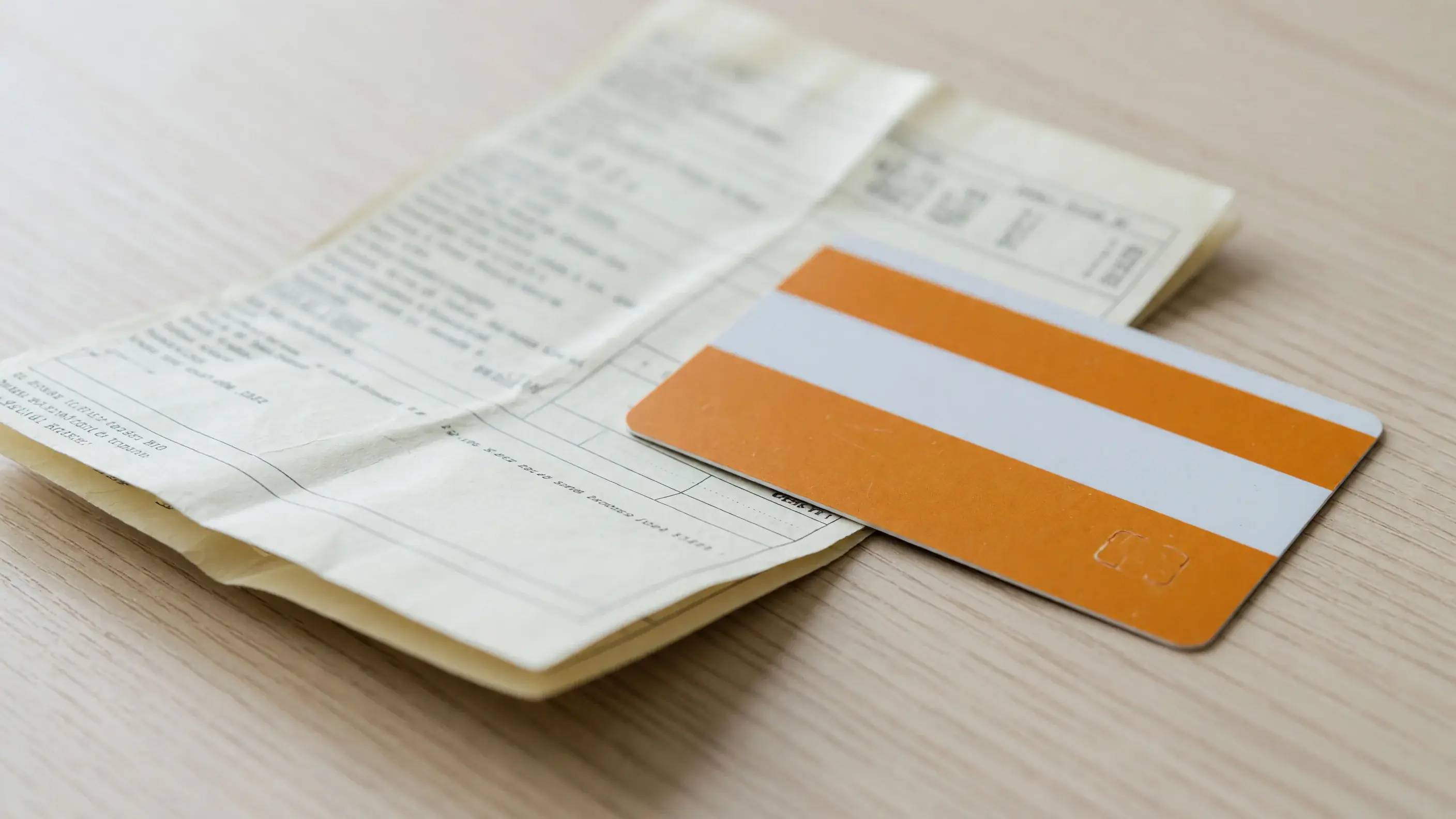 Cartão GOL Smiles BB Visa Infinite, em laranja e branco e sem marcas visíveis na face, apoiado sobre a fatura do mês em papel dobrada, fotografada em ângulo raso e sem texto legível.