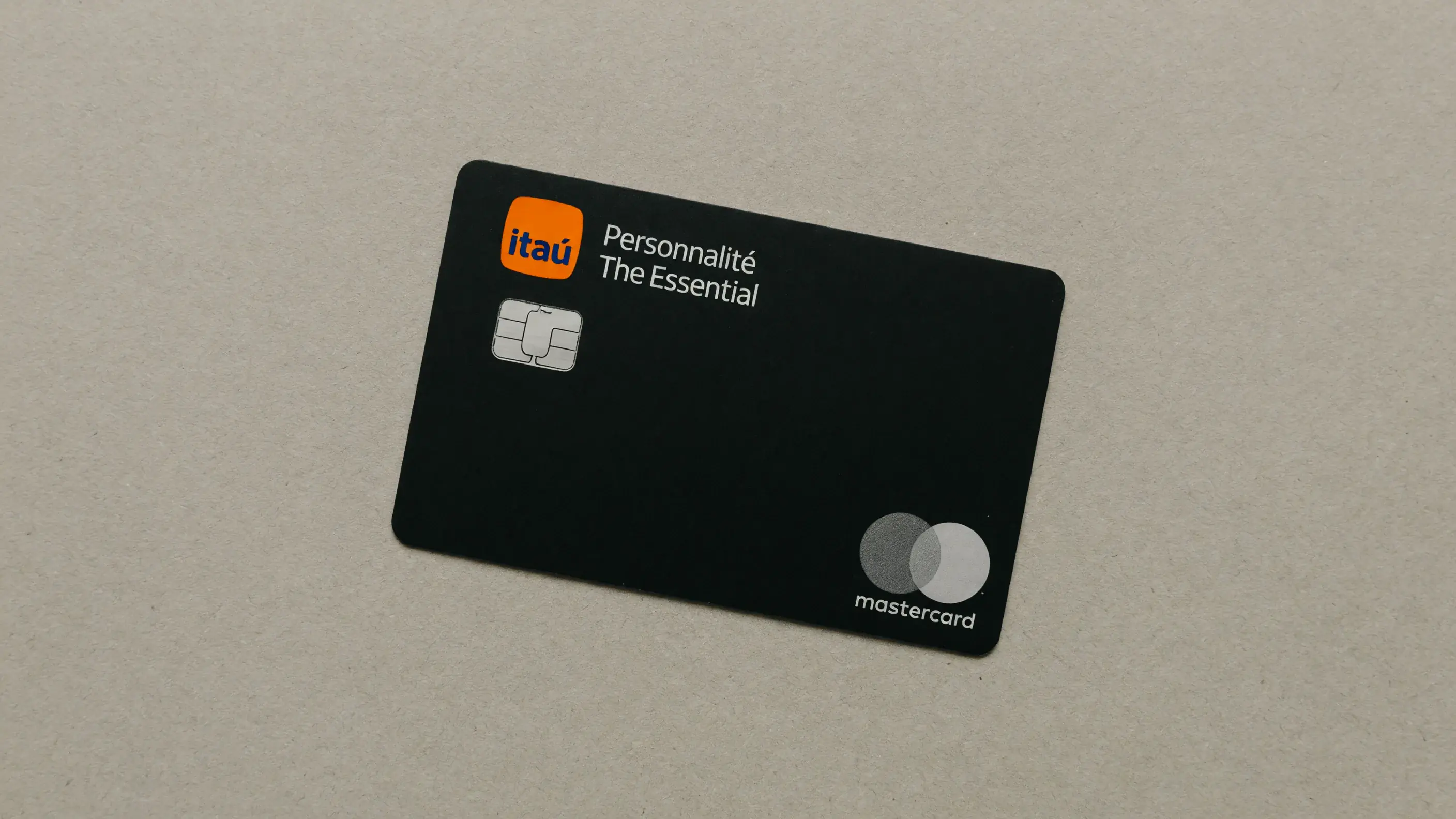 Cartão físico The Essential, o Mastercard Black do Itaú Personnalité, sozinho e de frente sobre uma superfície neutra, com o logotipo do Itaú, as palavras Personnalité e The Essential e a bandeira Mastercard na face