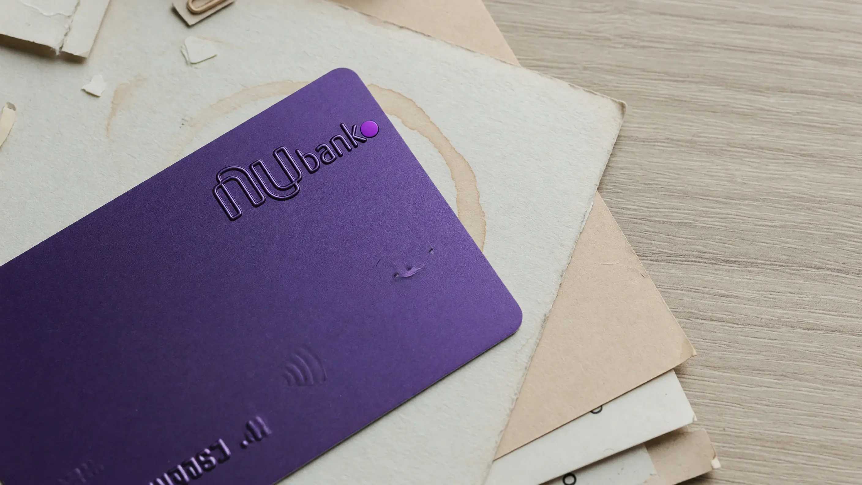 O cartão Nubank Ultravioleta, roxo e com o logotipo do Nubank em relevo, apoiado sobre uma mesa clara, sem número legível.
